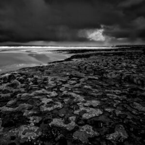 Zdjęcie pracy Małgorzaty Mikołajczyk. Fotografia przedstawia surowy krajobraz nad morzem lub oceanem i pochmurne niebo