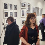 Zdjęcie z wernisażu wystawy iLand Małgorzaty Mikołajczyk. Kierowniczka galerii rozmawia z gośćmi, W ręku trzyma mikrofon