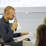 Zdjęcie z wieczoru poetyckiego Co kryje poezja obrazów Rafała Bakalarczyka. Prowadzący spotkanie, z kartką w ręku mówi w kierunku artysty.