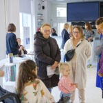 Sala wstawiennicza. Autorka wystawy - Paula Jaszczyk rozmawia z 4 kobietami w okularach. Wszyscy patrzą w kierunku małej dziewczynki