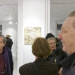 Wernisaż wystawy "Paint and Print?". Grupa ludzi rozmawia i podziwia prace.