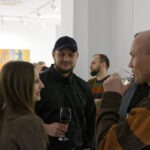 Wernisaż wystawy "Paint and Print?". Grupa ludzi rozmawia i podziwia prace.