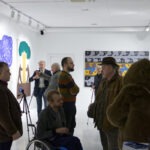 Wernisaż wystawy "Paint and Print?" Grupa ludzi rozmawia i podziwia prace.