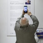 Wernisaż wystawy "Paint and Print?". Mężczyzna robi zdjęcie tekstu kuratorskiego.