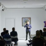 Spotkanie w Aptece Sztuki o nazwie "Sztuka Stand-upowania". Mężczyzna mówi do mikrofonu.
