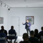 Spotkanie w Aptece Sztuki o nazwie "Sztuka Stand-upowania". Mężczyzna mówi do mikrofonu.